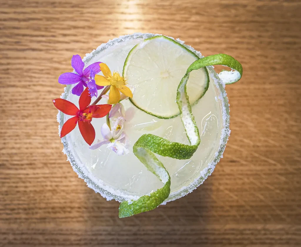 Overhead view of a margarita garnished with lime, flowers, and salt rim.