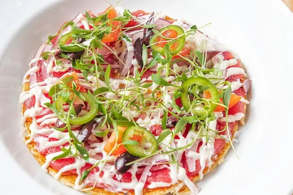 A flatbread with red meat, red onions, microgreens, jalapenos, and white sauce.