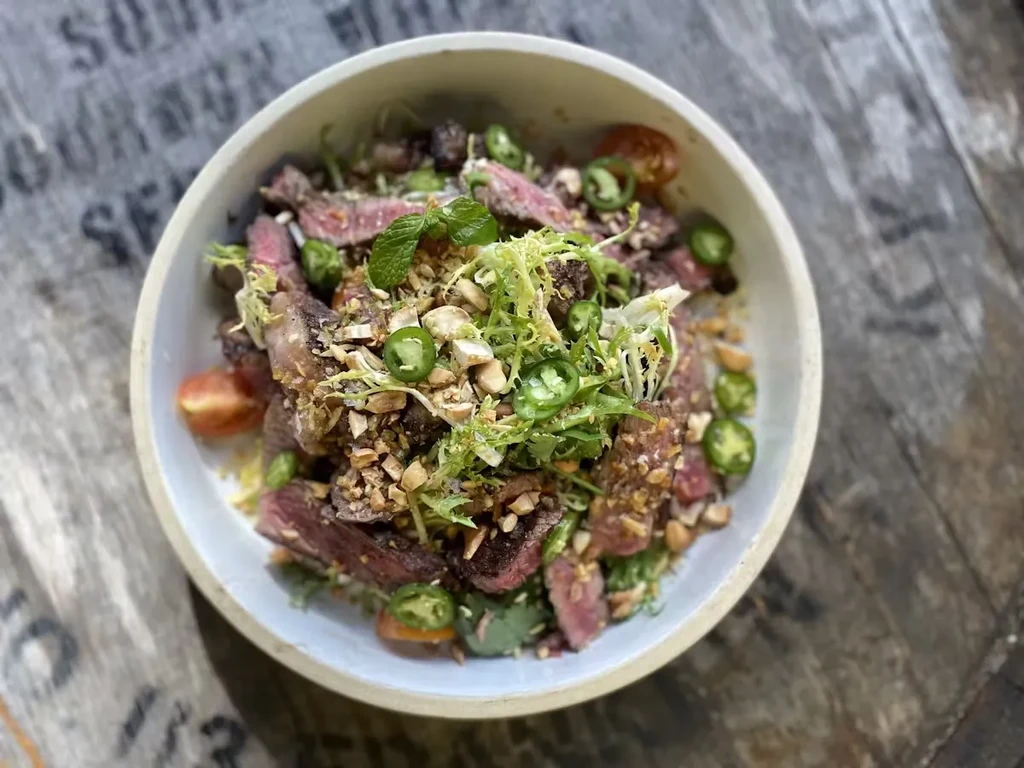 A bowl of steak salad with peanuts, jalapeños, and greens.