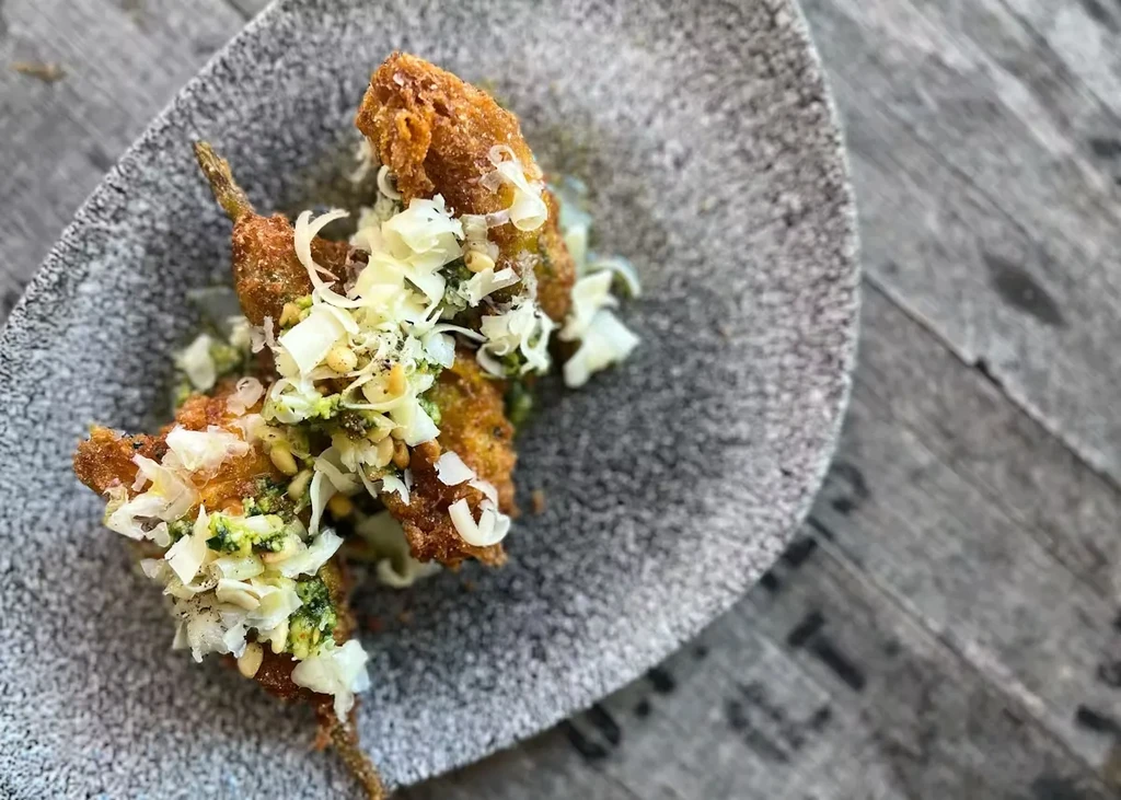 Fried vegetables with pesto, cheese, and pine nuts on a gray plate.
