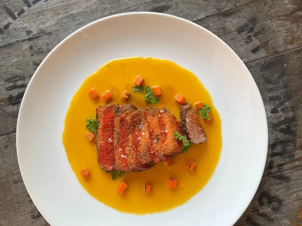 Sliced beef with a yellow sauce, carrots, and parsley on a white plate.