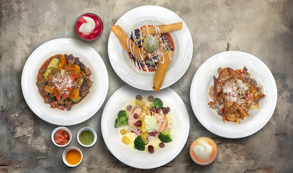 Overhead shot of four plates of Mexican food and two drinks on a table.