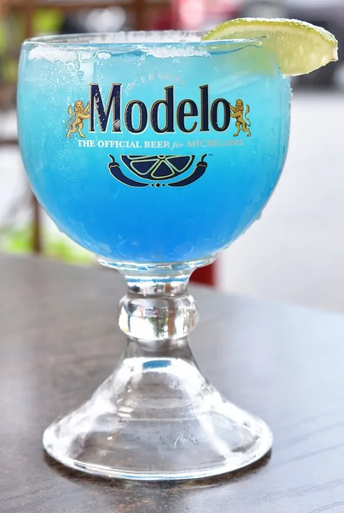 Blue Modelo drink with a lime wedge in a salt-rimmed glass.