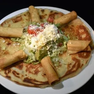 A large Mexican plate with crepes and taquitos surrounding a salad.