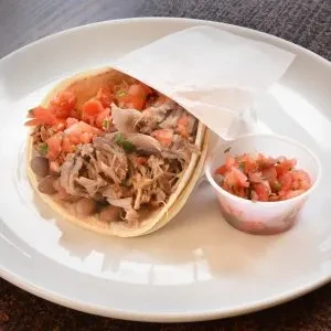 A pork carnitas taco with pico de gallo on a white plate.