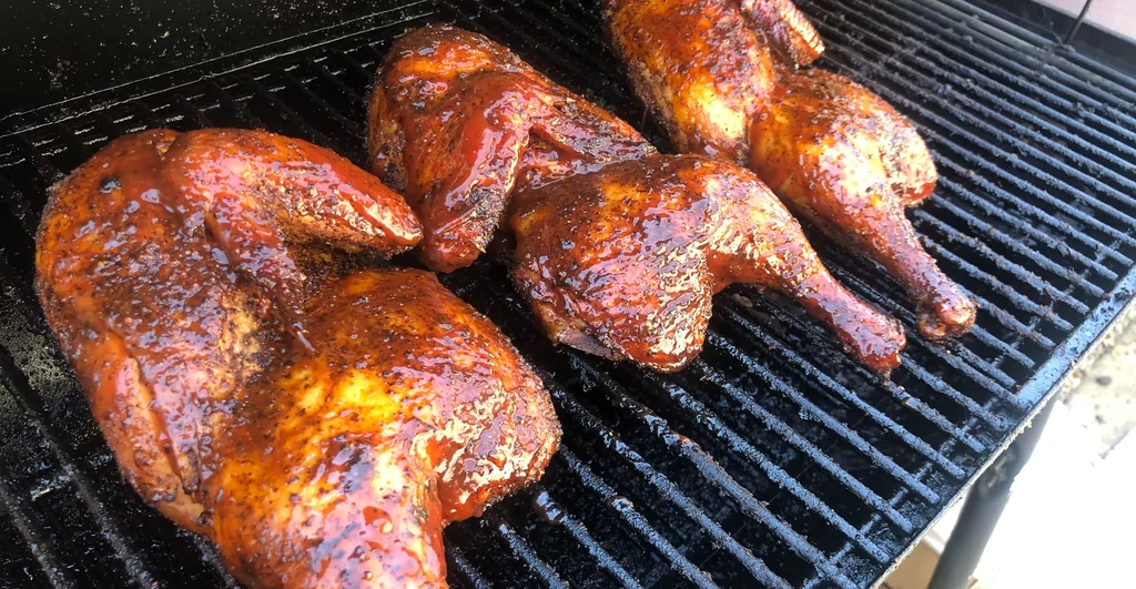 Barbecue chicken pieces, glistening with sauce, grilling on a dark grate.