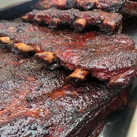 Close-up of several racks of barbecue ribs with dark, glossy crust.
