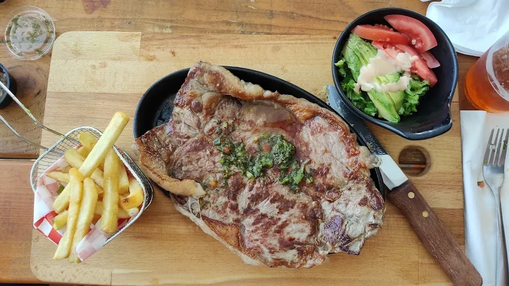 Top-down view of a steak, fries, and salad on a wooden board.