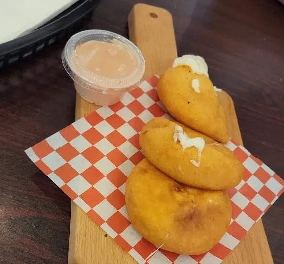 Three fried empanadas with sauce on a checkered paper on a wooden board.
