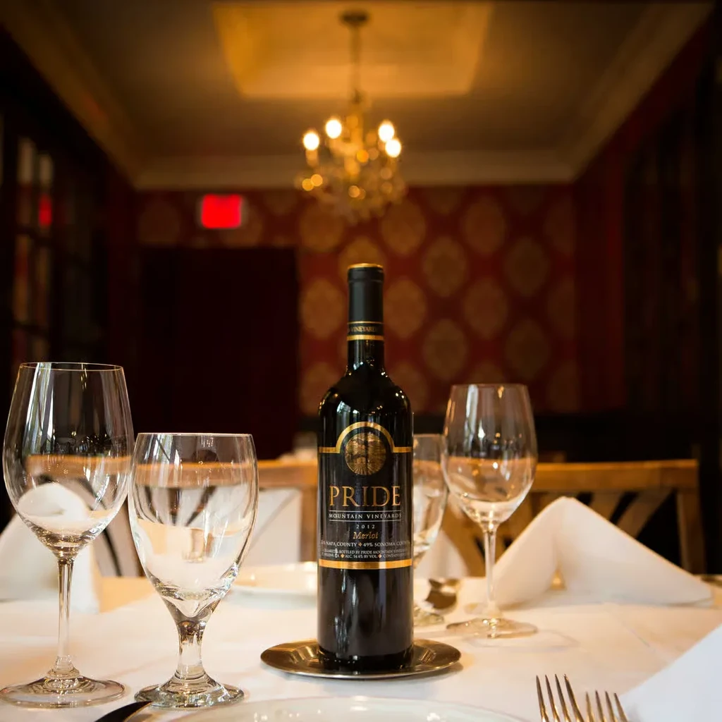 A bottle of Pride Merlot wine on a table with wine glasses.