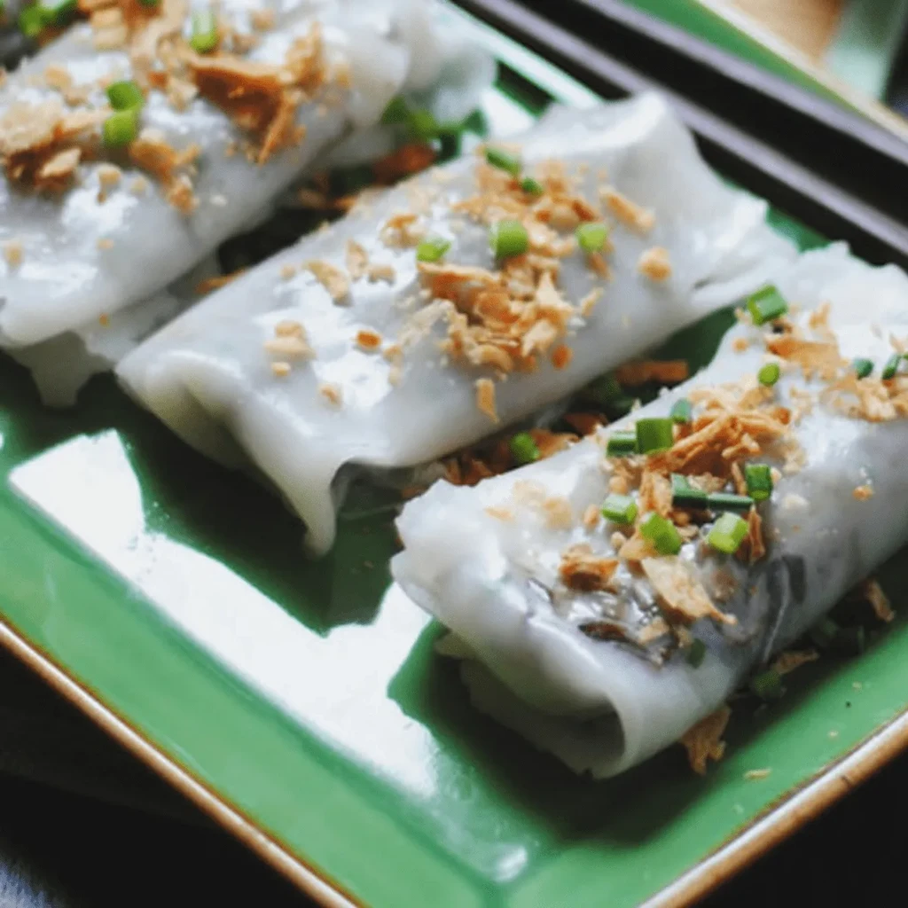 Three white steamed rolls topped with green onion and crispy onions on a green plate.