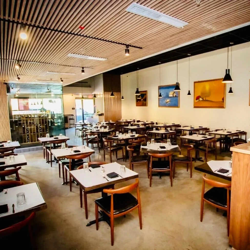 An empty restaurant with a beige wooden ceiling and abstract art.