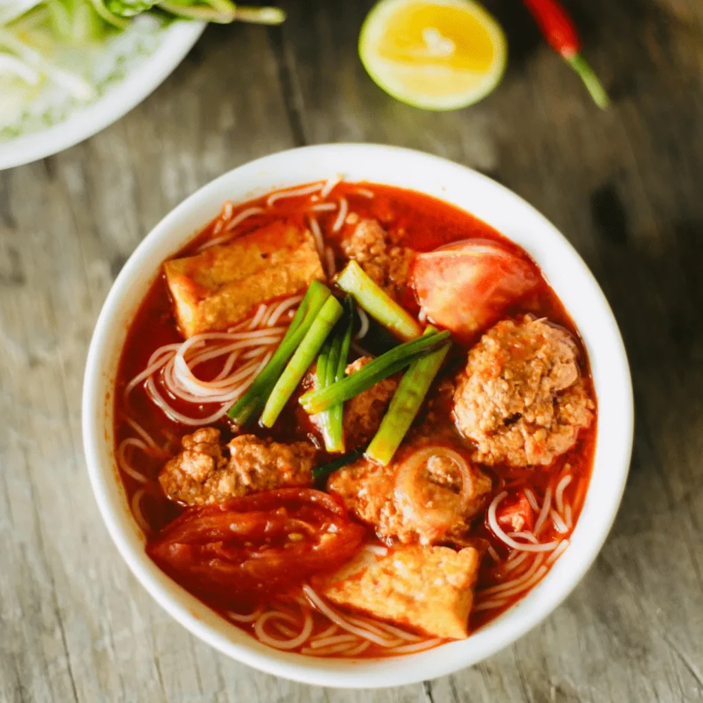 Vietnamese Bun Rieu soup with noodles, tofu, meat, tomatoes, and scallions.