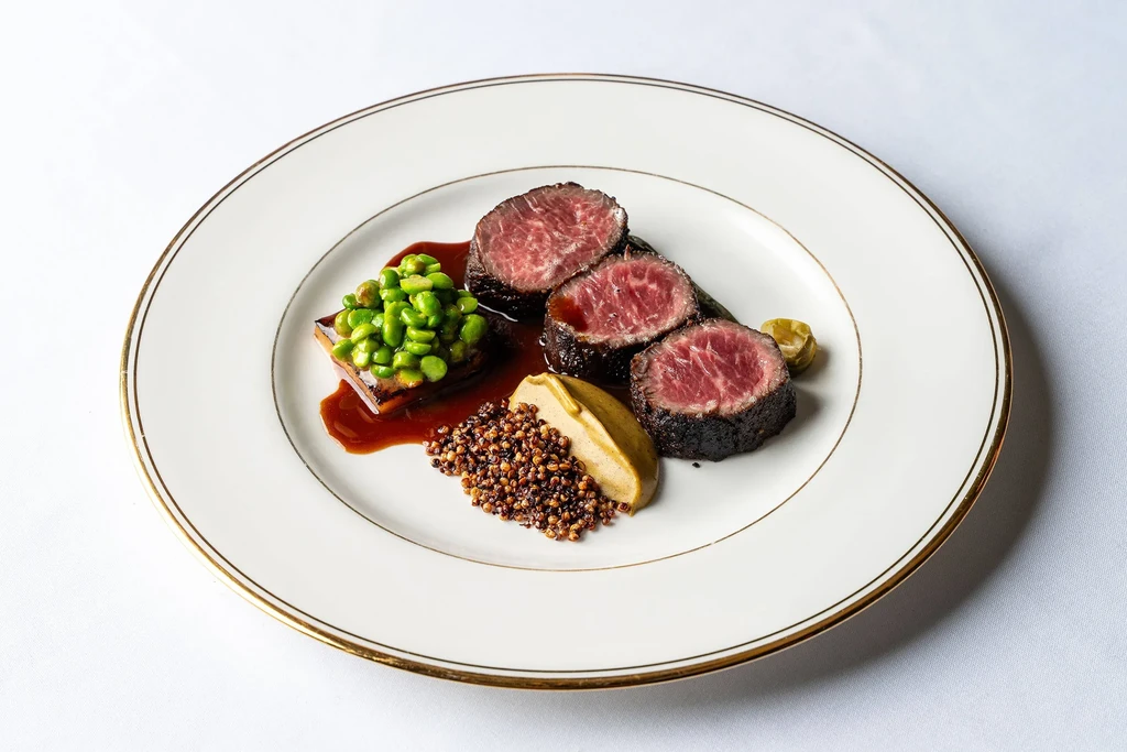 Slices of rare steak, peas, quinoa, and sauce on a white plate.