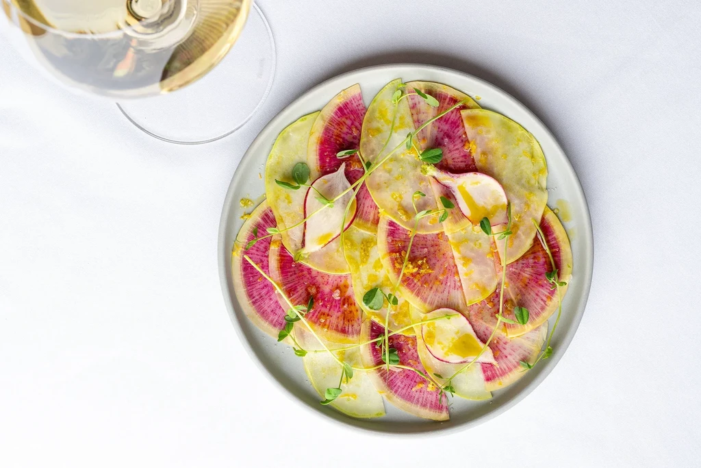 A plate of sliced pink and white radishes with oil and sprouts.