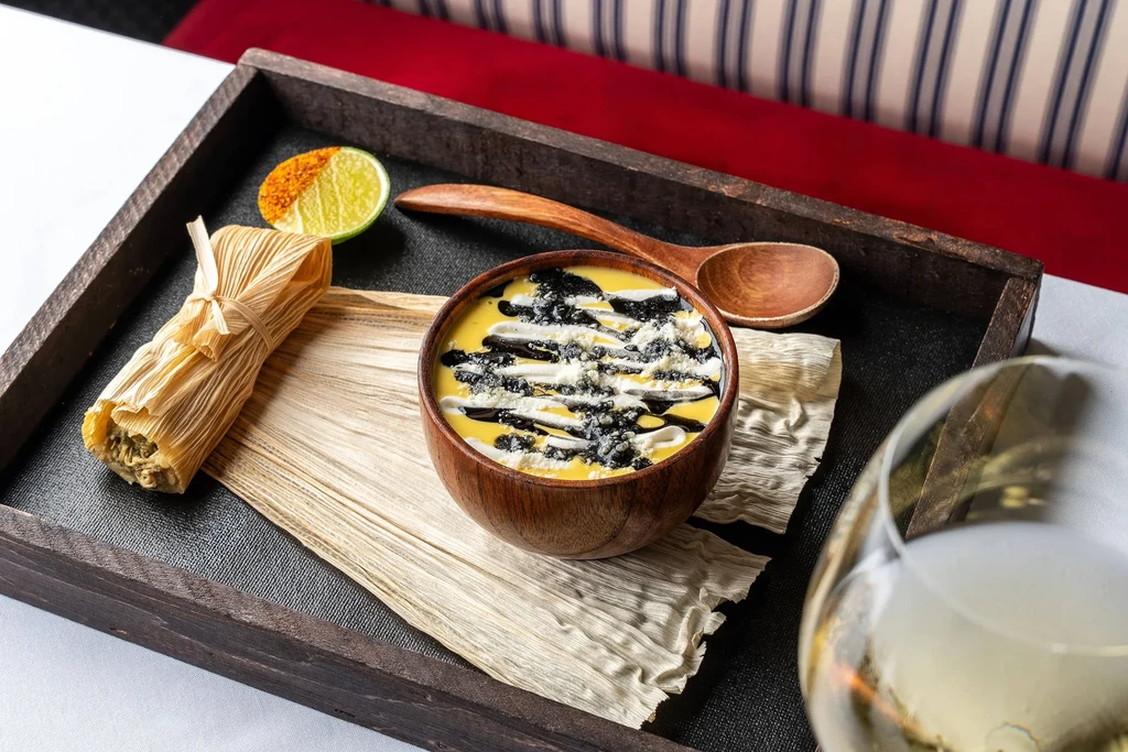 A tamale, a bowl of soup, and a lime on a serving tray.