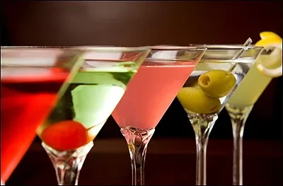 Five martini glasses with colorful cocktails, olives, and a lemon peel.