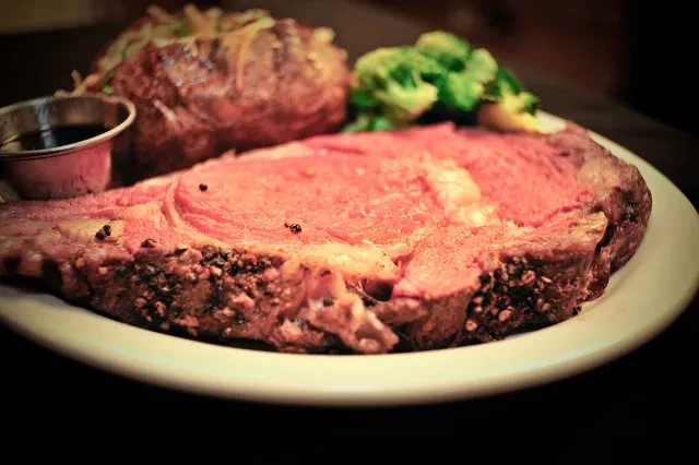 A close-up of a prime rib with baked potato and broccoli.