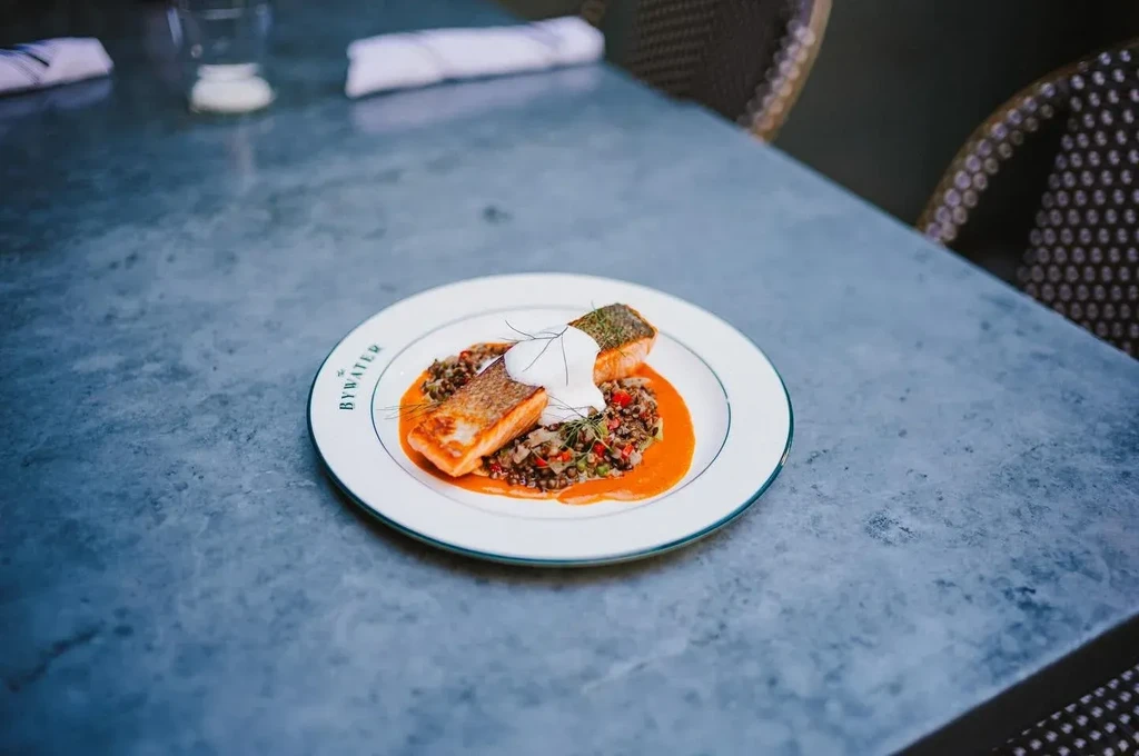 Two pieces of salmon on lentils and sauce on a white plate.