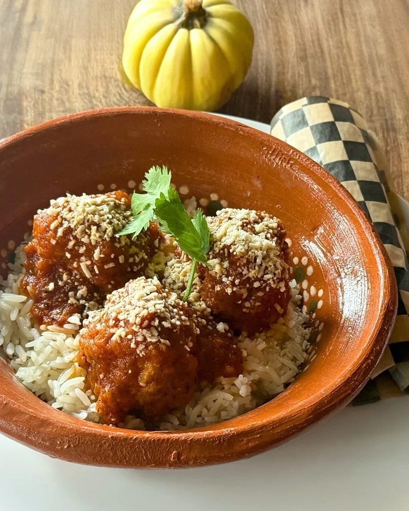 Meatballs in sauce over rice, topped with cilantro, in a terracotta bowl.