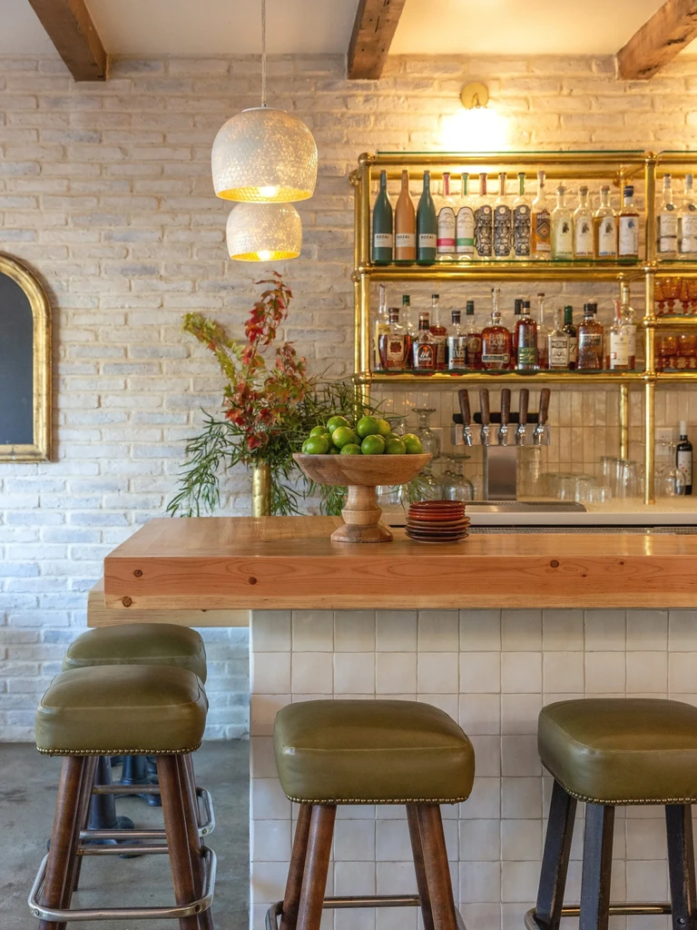 A modern bar with a wooden counter, green stools, and brick wall.