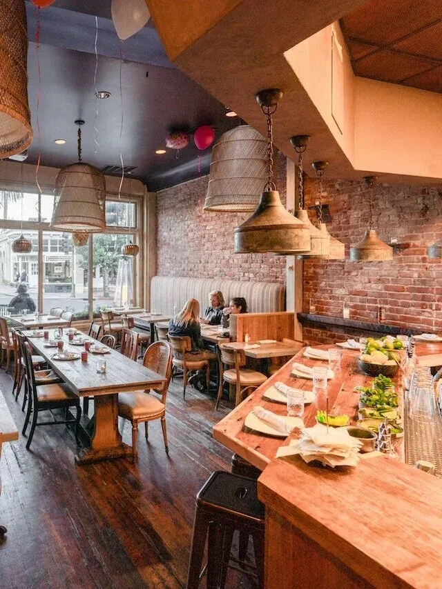 A rustic restaurant interior with brick walls, wooden tables, and hanging lights.