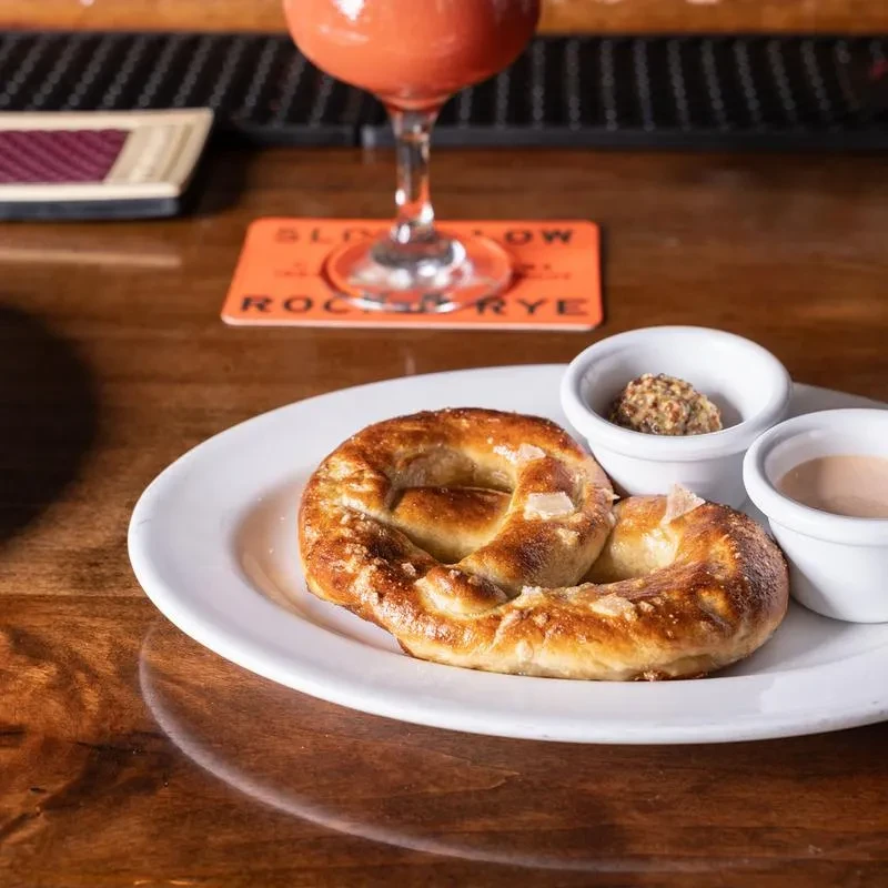 A salted pretzel on a white plate with two dipping sauces.