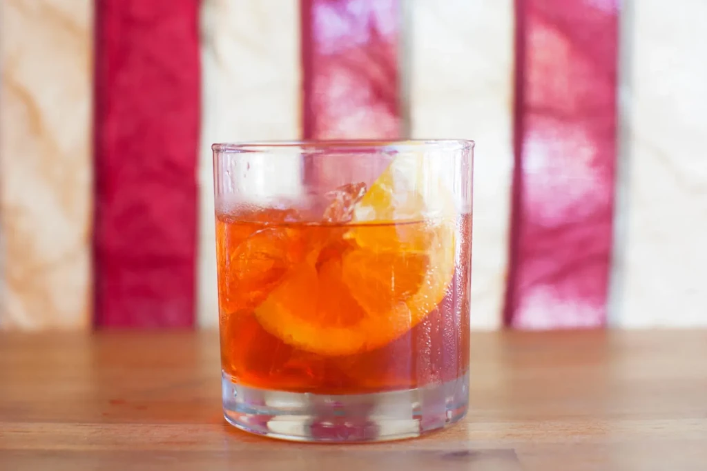 A glass of orange drink with orange slices and ice.