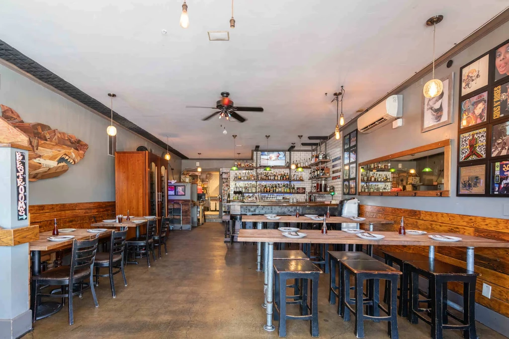 Rustic-industrial restaurant interior with a bar, high tables, and album art.