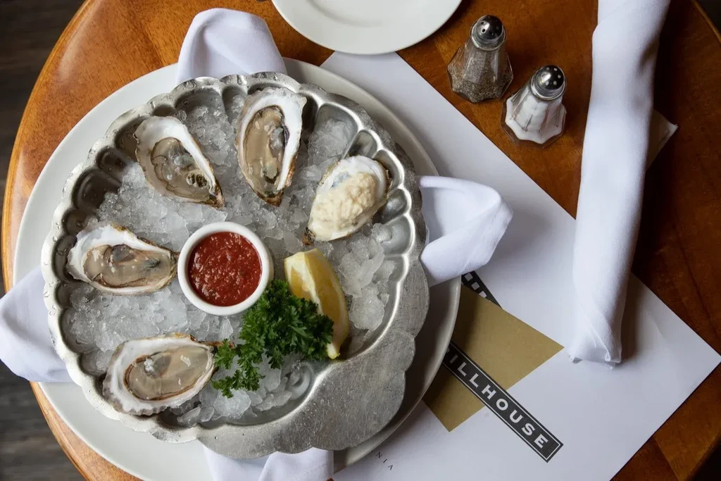 A silver platter of fresh oysters on ice with sauce and lemon.