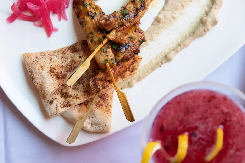 Chicken skewers with pita, hummus, pickled onions, and a pink drink.