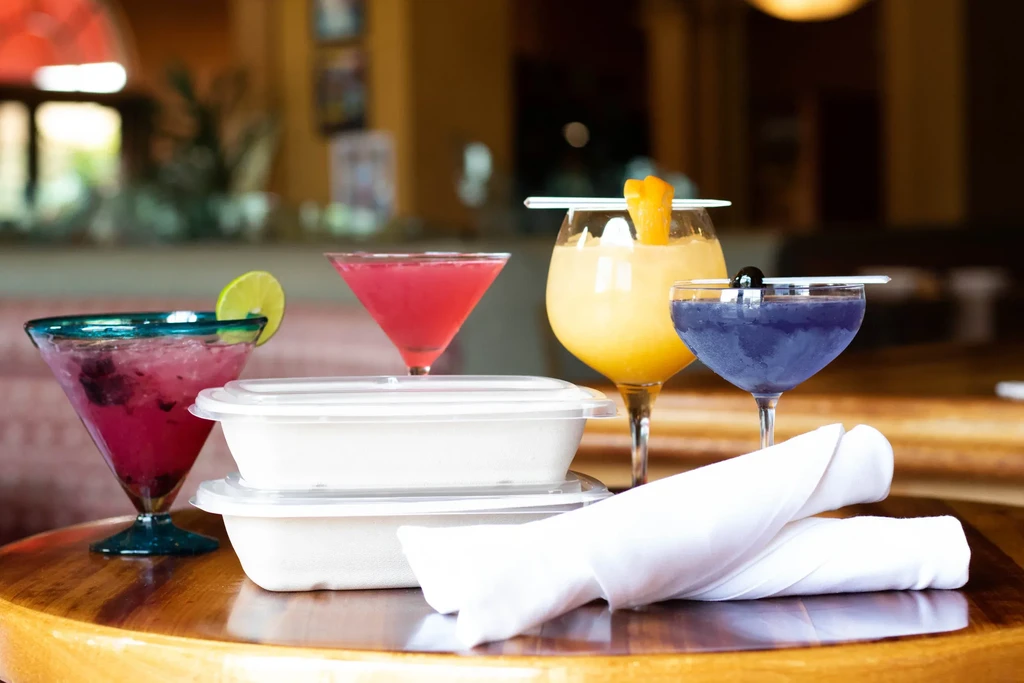 Four colorful cocktails, two takeout containers, and two white napkins on a table.