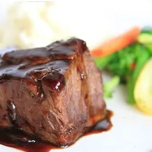A chunk of beef with gravy, mashed potatoes, and vegetables.