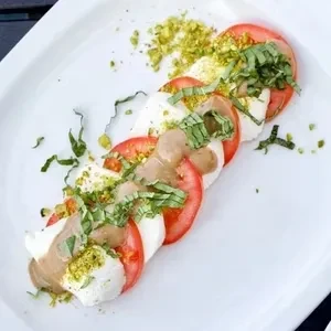 Caprese salad with sliced tomatoes, mozzarella, pesto, and balsamic glaze.