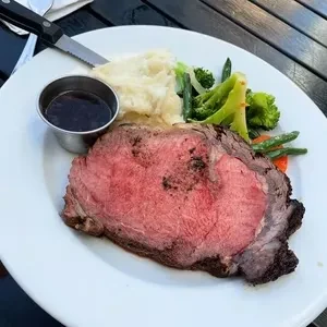 A plate of rare prime rib with mashed potatoes and mixed vegetables.