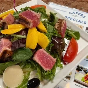 Seared tuna, mango, and greens salad on a white plate.