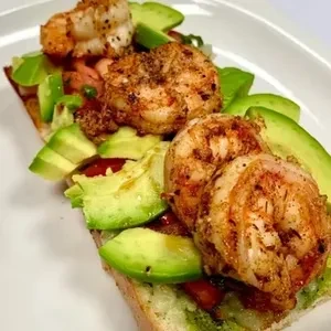 Toasted bread topped with seasoned shrimp, avocado slices, and diced tomatoes.