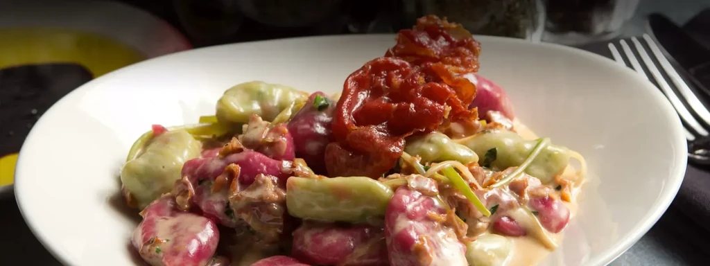 Red and green pasta with bacon in cream sauce on a white plate.