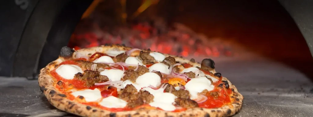 Pizza with sausage, mozzarella, and onions baking in a wood-fired oven.