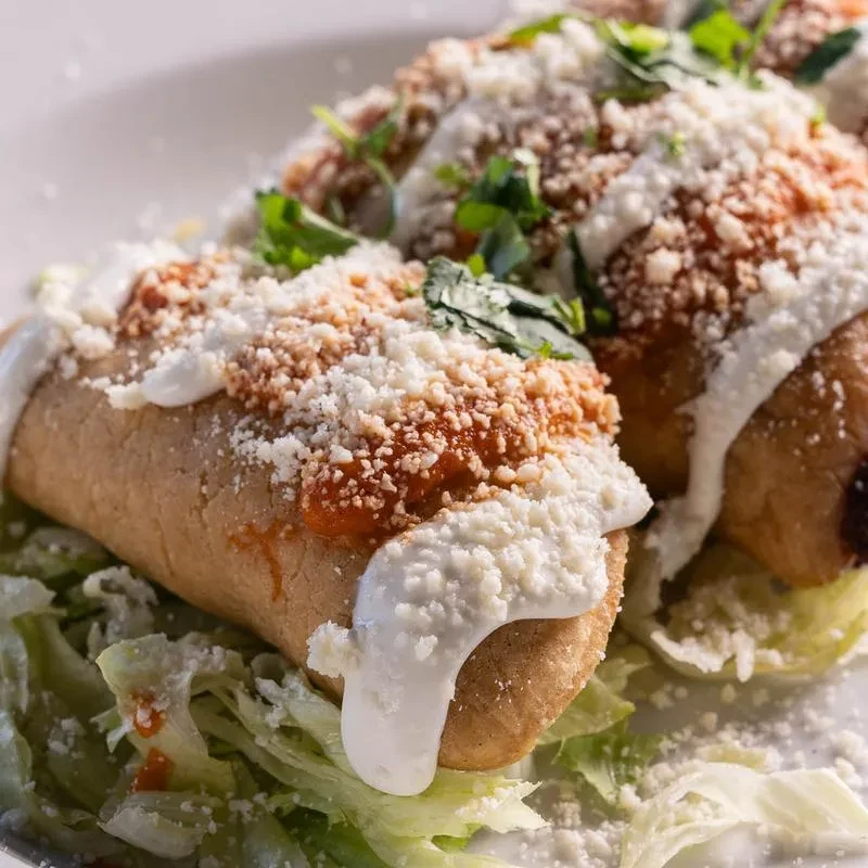 Two tamales topped with sauce, cheese, cream, and cilantro on lettuce.