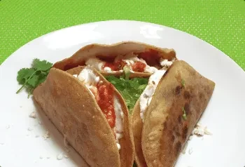 Three fried tacos with cheese and red salsa on a white plate.
