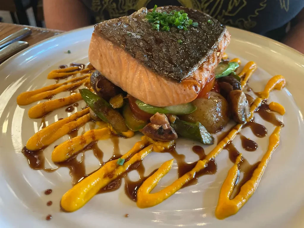 Salmon fillet with vegetables, sauces, and chives on a white plate.