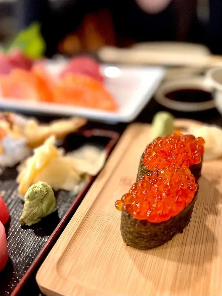 Two pieces of ikura gunkan sushi on a bamboo plate.