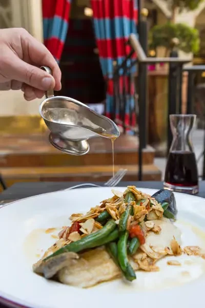 Hand pouring sauce from a silver gravy boat onto a meal.
