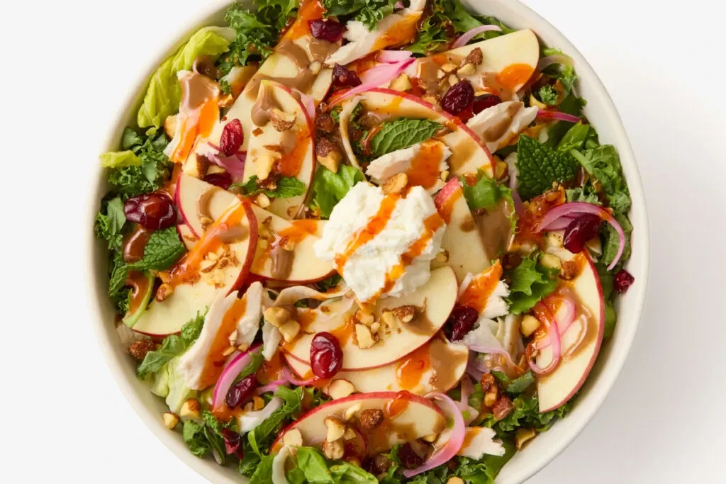 Top-down view of a salad with apples, goat cheese, cranberries, and dressing.