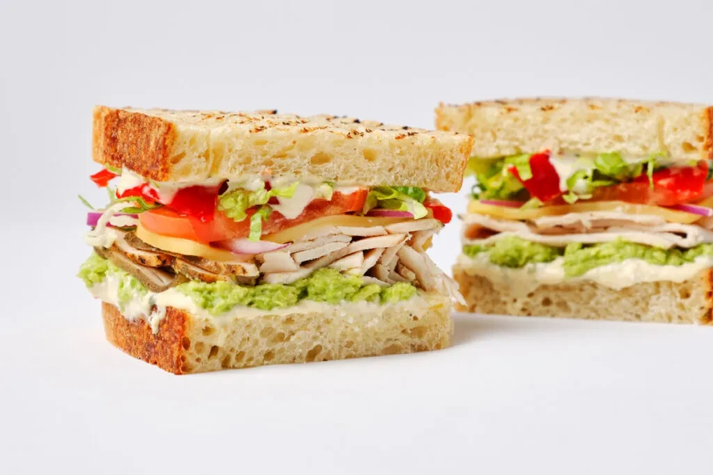 Two hearty sandwiches with turkey, cheese, avocado, tomato, and lettuce.