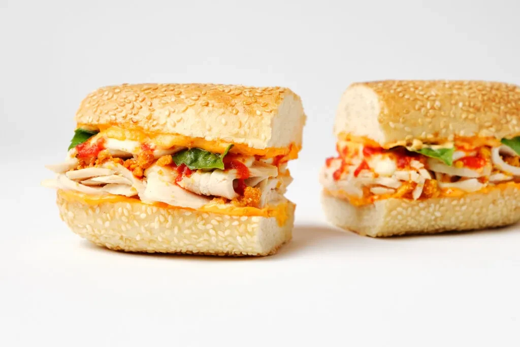 Two sliced chicken sandwiches on sesame seed buns, white background.