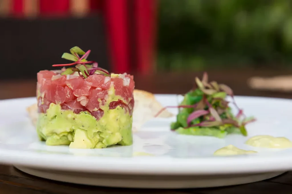 A tuna and avocado tartare with microgreens on a white plate.