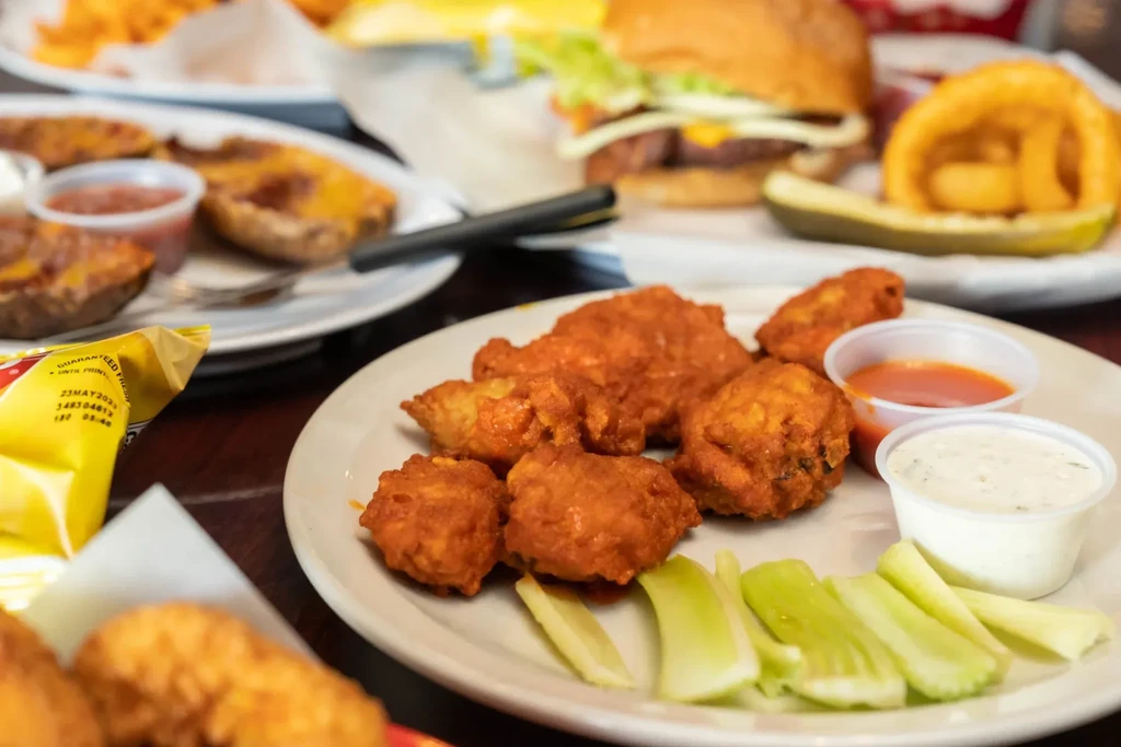 A plate of buffalo wings with celery sticks and dipping sauces.