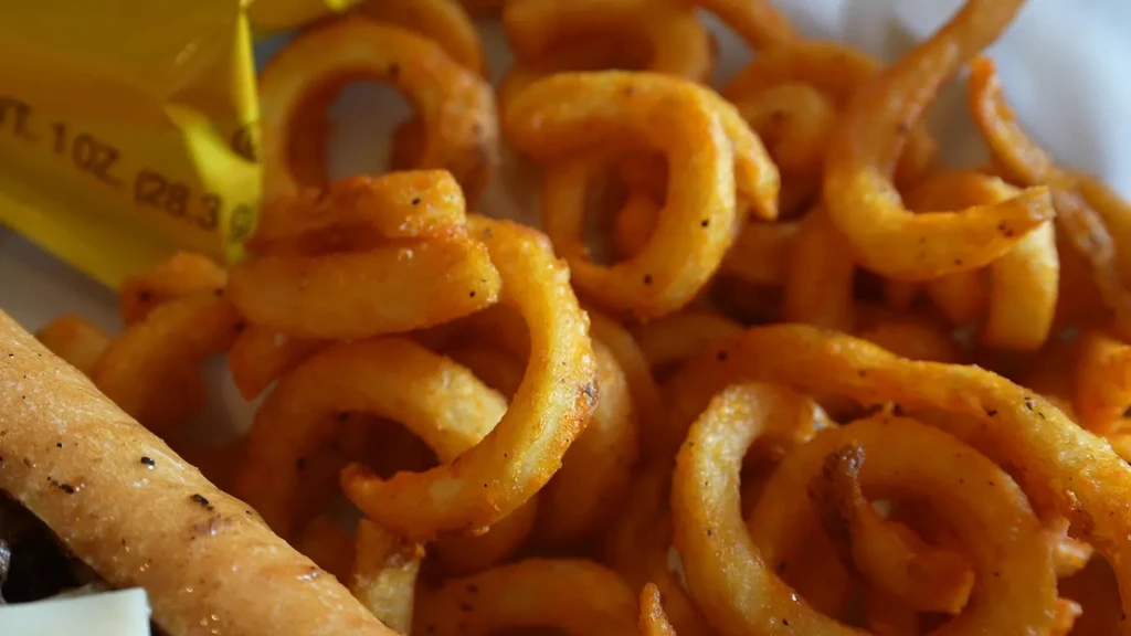 A close-up of seasoned curly fries and a breadstick.